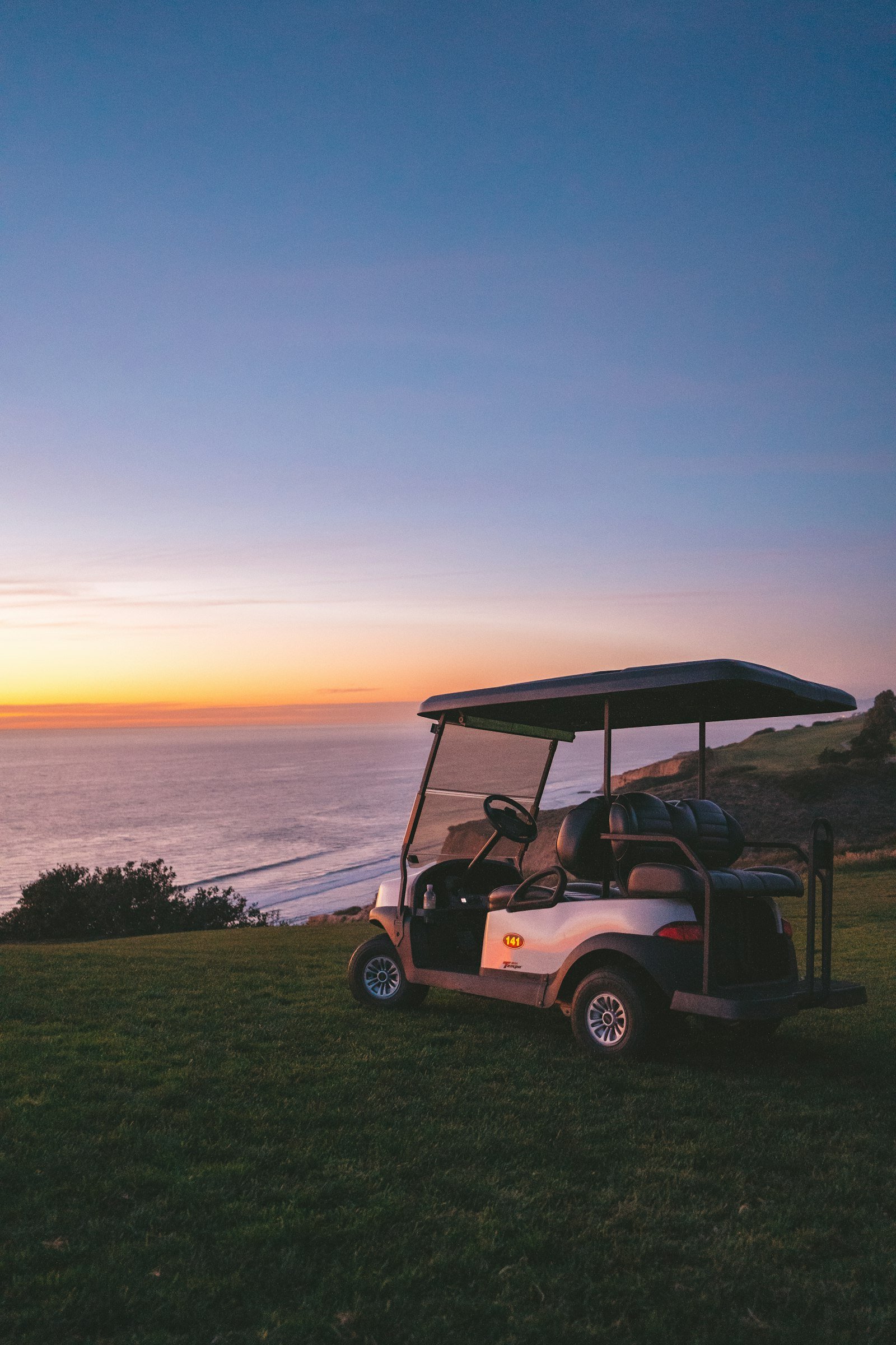 Golf cart parked on a bluff above the ocean at sunset